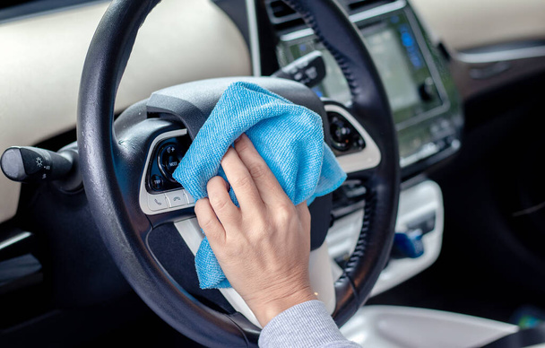 car wash and interior chemical cleaning concept.hand use microfiber cloth and spray to clean lateral door from inside,retractable rear view mirror,steering wheel.modern hybrid vehicle clean inside - Foto, imagen