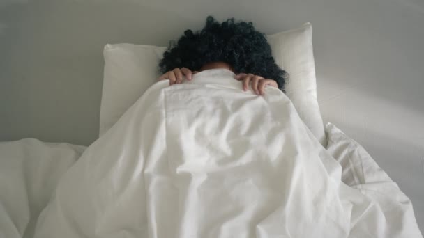 Top view close up woman of color with dark curly hair surprisingly open mouth on sunny morning 4K slow motion. Happy playful African American woman peeking out from blanket in bed, smiling to camera - Video