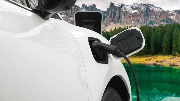 電気発生器ドライブによるエネルギー持続可能な車の電源、プログレッシブ旅行の概念のための山の背景と充電ステーションでバッテリーを充電します。クリーン環境のシンボルとして自然界のEV車. - 写真・画像
