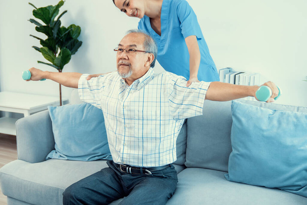Contented senior patient doing physical therapy with the help of his caregiver. Senior physical therapy, physiotherapy treatment, nursing home for the elderly - Photo, image
