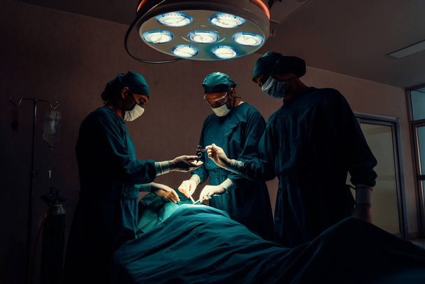 Équipe chirurgicale effectuant une intervention chirurgicale au patient en salle d'opération stérile. Dans une salle d'opération éclairée par une lampe, une équipe chirurgicale professionnelle et confiante fournit des soins médicaux à un patient inconscient. - Photo, image