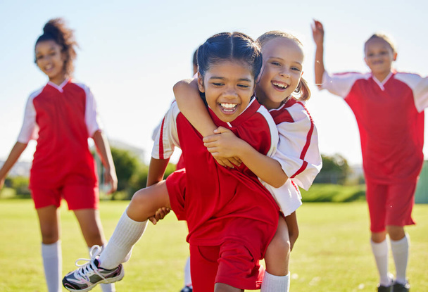 Soccer, girl celebration and field with happy piggyback, team building support and solidarity for winning game. Female kids, sports diversity and celebrate with friends, teamwork and goal in football. - Photo, image