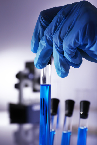 Artículos de vidrio de laboratorio con líquido azul en la mano del científico sobre fondo gris
 - Foto, Imagen