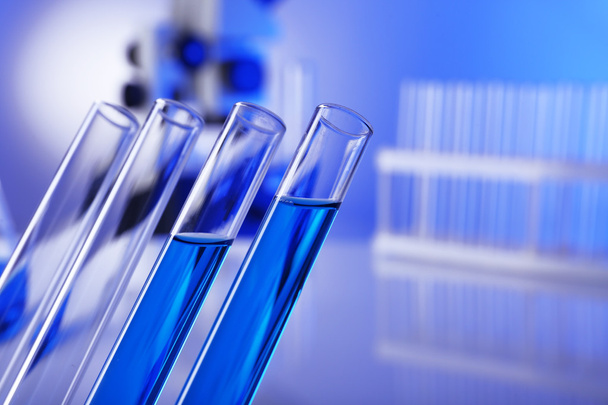 Laboratory glassware with blue liquid on bright background - Zdjęcie, obraz