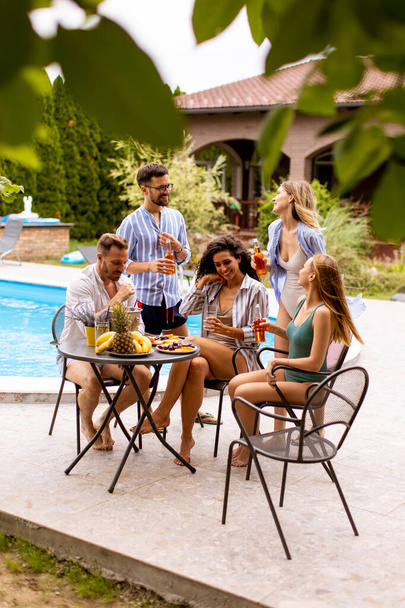 Група щасливих молодих людей, що вітають з сидінням біля басейну в саду
 - Фото, зображення