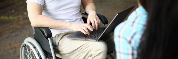 Man in wheelchair and woman work remotely while sitting in park. Freelance for people with disabilities concept - Photo, image