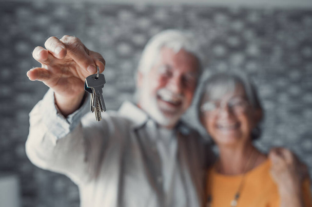 Close up focus of happy old Caucasian couple show keys to own apartment or house. Smiling mature retired man and woman celebrate relocation to new home. Moving, rental, estate concept. - Photo, Image