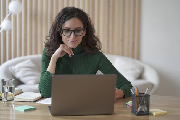 Młoda miła Włoszka freelancer pracuje na laptopie zdalnie z domu, atrakcyjna hiszpańska kobieta w okularach studiuje online lub robi zakupy w sklepie internetowym. Koncepcja wolnego strzelca - Zdjęcie, obraz