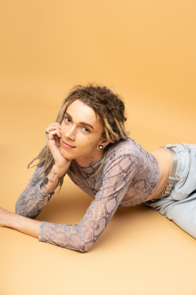 Smiling tattooed queer person in top looking at camera on yellow background  - Zdjęcie, obraz