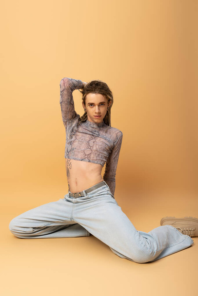 Trendy nonbinary person in crop top posing while sitting on yellow background  - Foto, Imagem