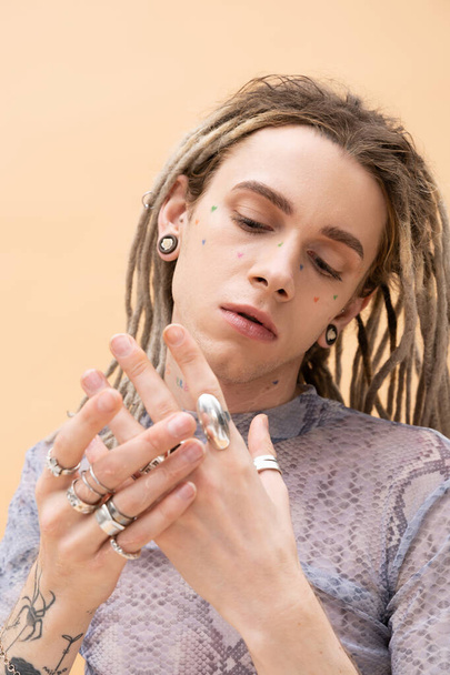 Portrait of nonbinary person touching silver rings on fingers isolated on yellow  - Φωτογραφία, εικόνα