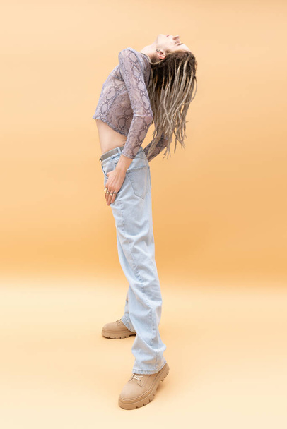 Side view of stylish queer person with dreadlocks posing on yellow background  - Φωτογραφία, εικόνα