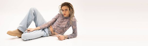 Queer person with dreadlocks looking at camera while lying on white background, banner  - Fotó, kép