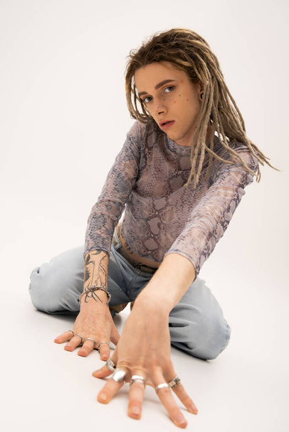 Tattooed queer person with rings on fingers looking at camera on white background - Fotó, kép
