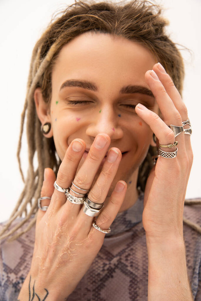 Smiling tattooed queer person with silver rings isolated on white  - Фото, изображение