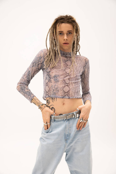 Tattooed nonbinary person in crop top touching jeans isolated on white  - Foto, Bild
