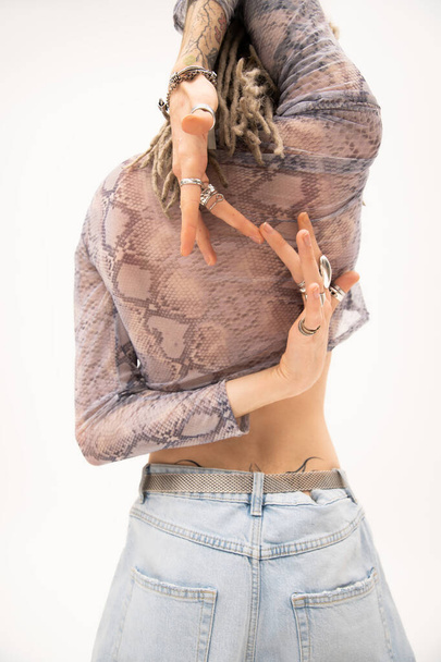 back view of nonbinary person in snakeskin print top and silver rings posing with hands behind back isolated on white - Zdjęcie, obraz