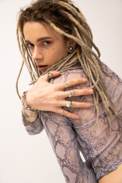 young queer person with dreadlocks and silver finger rings looking at camera isolated on white - Fotó, kép