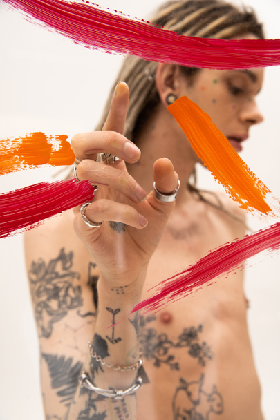 colorful paint strokes on glass near blurred nonbinary person pointing with finger on white background - Fotografie, Obrázek
