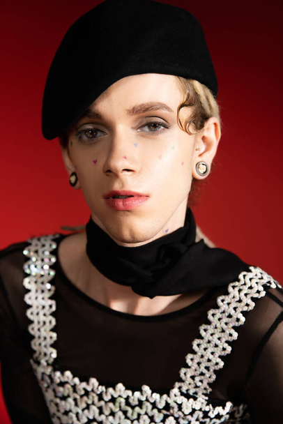 portrait of elegant nonbinary model in black beret and neckerchief looking at camera on red background - Φωτογραφία, εικόνα