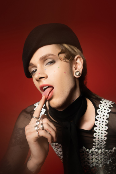 queer person in elegant attire sticking out tongue and looking at camera on red background - Foto, Imagem