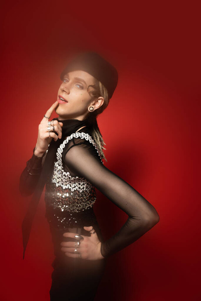 elegant queer model in black beret touching lip while posing with hand on hip on red background - Fotoğraf, Görsel