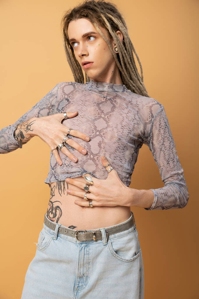 tattooed queer person with dreadlock posing in top with snakeskin print isolated on yellow - Foto, immagini