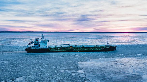 Enorme buque de carga navegando a través del agua del océano con gruesa capa de trozos de hielo rotos cubriendo la superficie en la vista aérea del día polar - Foto, Imagen