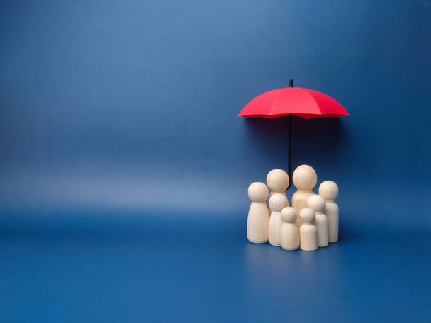 A family of wooden dolls are hiding under a red umbrella, protecting wooden peg dolls, planning, saving families, preventing risks and crises, health care and insurance concepts. - Foto, Imagem