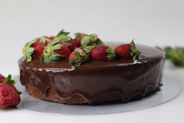 Chocolate cake with ganache and fresh strawberries. Shot on white background along with fresh strawberries around. - Photo, image