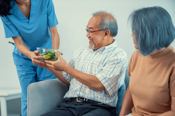 Жіноча медсестра подає чашу салату задоволеній старшій парі. Охорона здоров'я та медична допомога для літніх людей, будинок престарілих для пенсіонерів
. - Фото, зображення