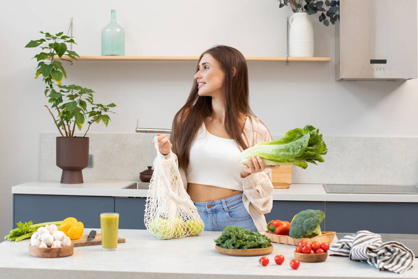 An attractive brunette pulls fresh vegetables out of a reusable bag. The concept of healthy eating. Vegetarianism. - Φωτογραφία, εικόνα