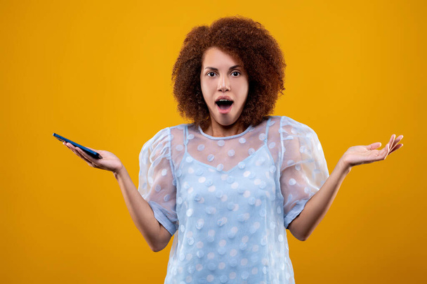 In shock. Young woman with a phone in hands looking surprised and shocked - Foto, Imagen