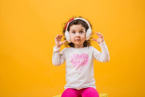 Little cheerful happy beautiful girl standing isolated on a yellow background in soft headphones, childish emotions. your text here - Fotoğraf, Görsel