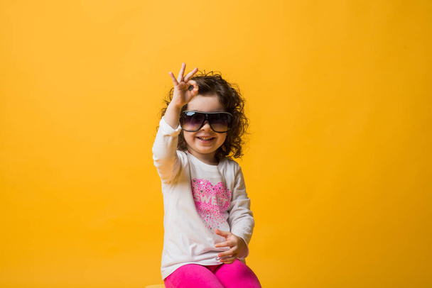 Little cheerful happy beautiful girl standing isolated on a yellow background in soft headphones, childish emotions. your text here - Fotografie, Obrázek