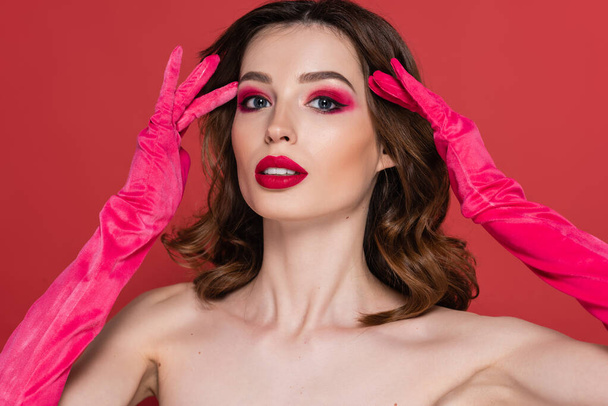 portrait of young woman with magenta color eye shadow posing in trendy gloves isolated on pink  - Foto, imagen