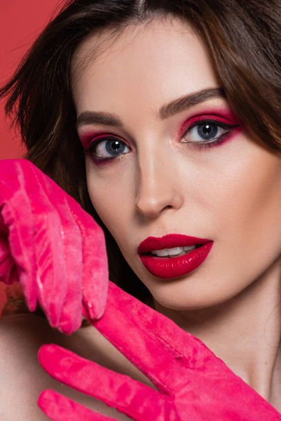 portrait of young woman with magenta color eye shadow pulling glove isolated on pink  - Photo, Image
