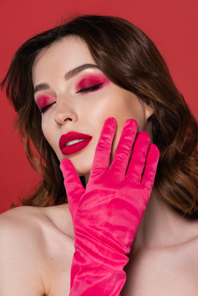 portrait of brunette woman with magenta color glove touching face isolated on pink  - Zdjęcie, obraz