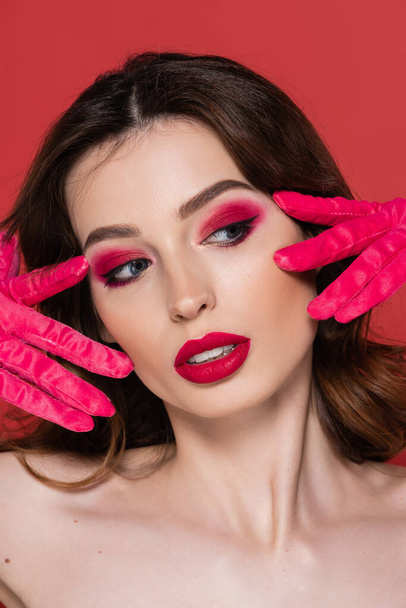 portrait of young woman with magenta color eye makeup posing in bright gloves isolated on pink  - Foto, immagini