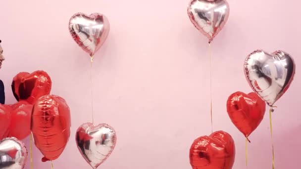 Beautiful couple on Valentine's Day celebrate February 14, love. Woman and man kissing behind balloons red hearts, romantic date, hug, cute - Filmagem, Vídeo