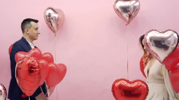 Beautiful couple on Valentine's Day celebrate February 14, love. Woman and man kissing behind balloons red hearts, romantic date, hug, cute - Πλάνα, βίντεο