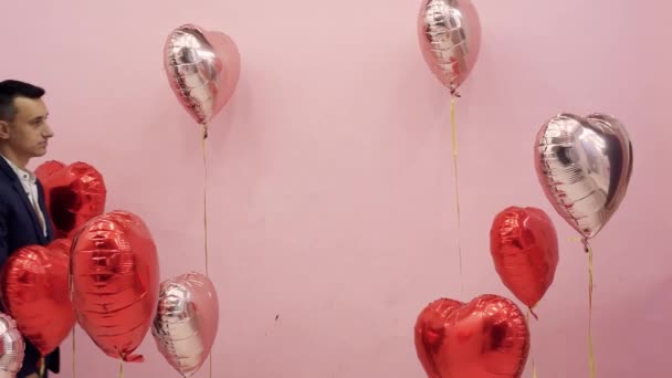Bella coppia a San Valentino festeggiare il 14 febbraio, amore. Donna e uomo che si baciano dietro palloncini cuori rossi, appuntamento romantico, abbraccio, carino - Filmati, video
