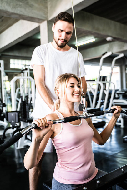 Спортсмен тренує жінку займатися фізичними вправами, піднімаючи вагу у спортивному тренажерному залі
 - Фото, зображення