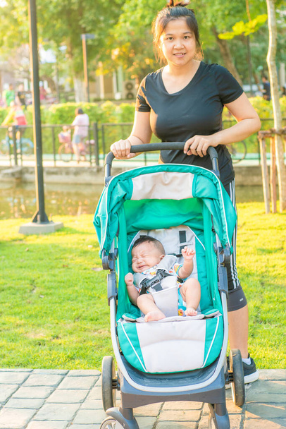 Ασιάτισσα μαμά που χρησιμοποιεί καροτσάκι με τον μικρό στο πάρκο - Φωτογραφία, εικόνα
