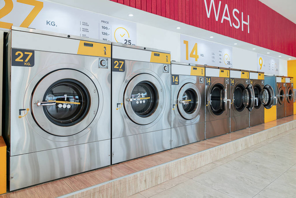 Μια σειρά από αναγνωρισμένα πλυντήρια ρούχων που λειτουργούν με κέρματα σε δημόσιο κατάστημα. Έννοια της self service εμπορική πλυντήριο και στεγνωτήριο ρούχων σε δημόσιο χώρο. - Φωτογραφία, εικόνα