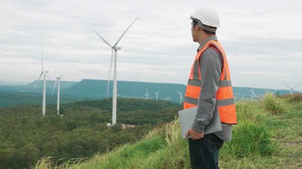 田舎の丘や山の上の風力発電所で働くエンジニア。再生可能エネルギー、持続可能なエネルギーの将来の生産のための進歩的な理想。風力タービンからの発電. - 映像、動画