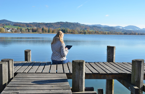 Mädchen liest Tablet gegen See. - Foto, Bild