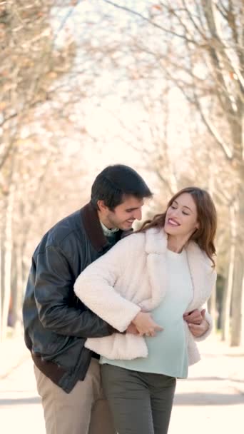 Щаслива вагітна пара обіймає, цілує і торкається її живота, дивлячись один на одного в парку. Вагітність
. - Кадри, відео