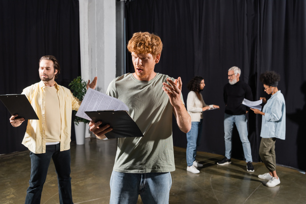 young men holding clipboards with screenplays and gesturing during rehearsing in theater - 写真・画像