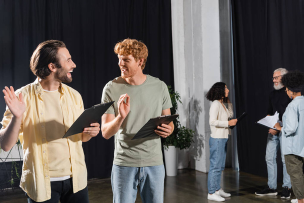 happy young actors with clipboards gesturing during rehearsal in acting skills school - Photo, Image